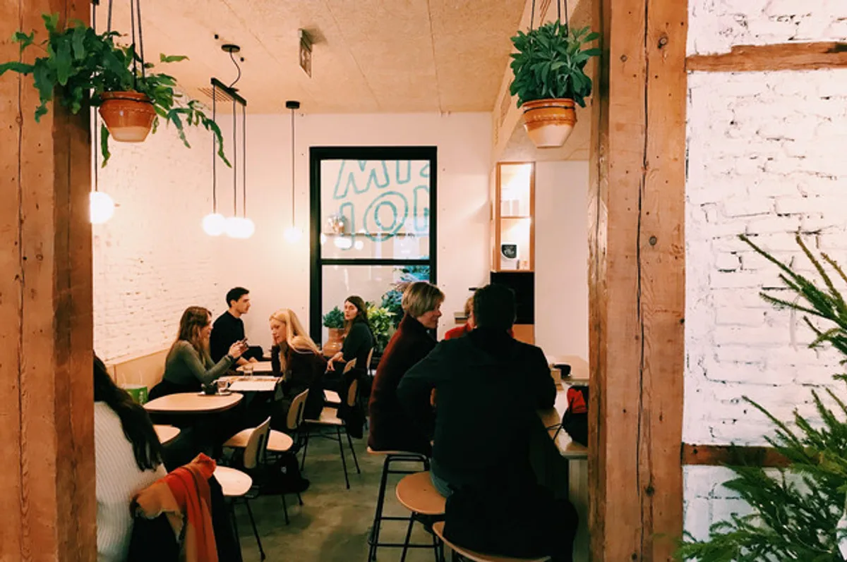Spacious interior of Misión Café, a contemporary cafe in Madrid with white brick walls, wooden beams, and ample seating, providing a productive atmosphere for one of the best work-friendly study spots in Madrid.