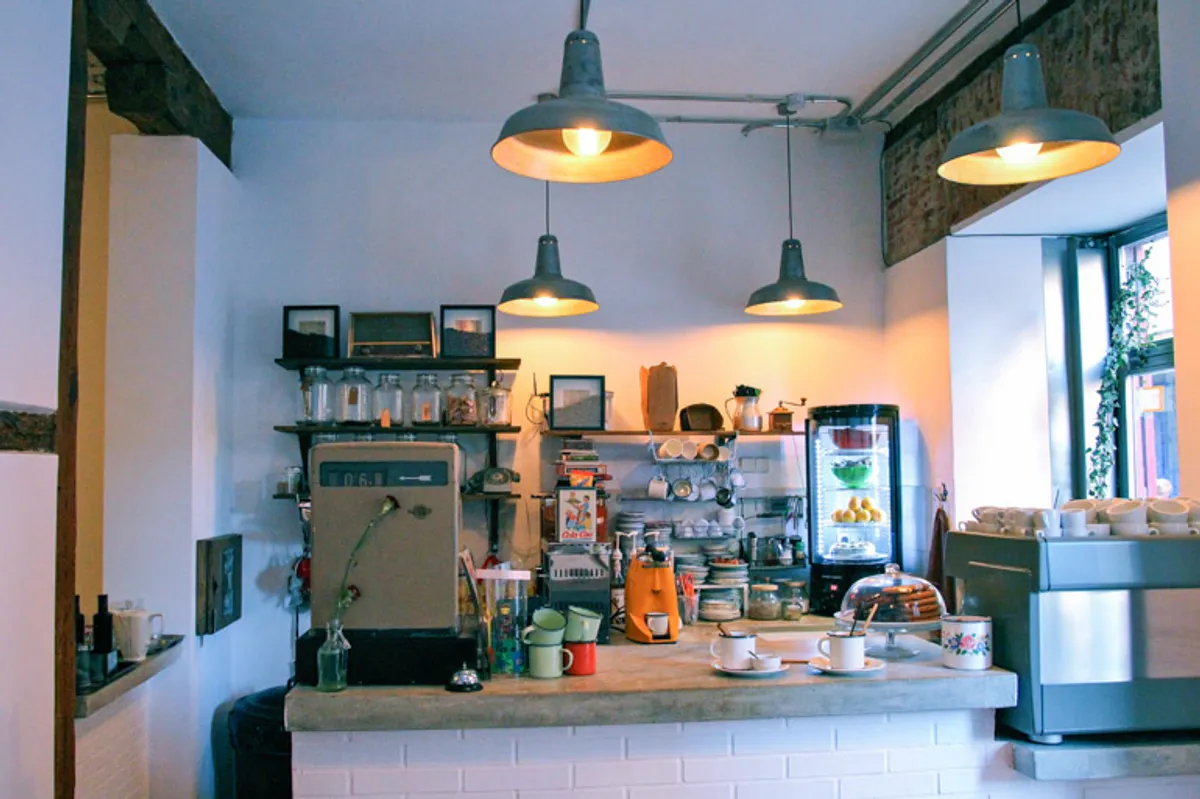 Eclectic interior of Cafelito cafe in Madrid featuring a white brick counter, industrial pendant lighting, and vintage coffee equipment, providing a creative atmosphere for those seeking unique study spots in Madrid.