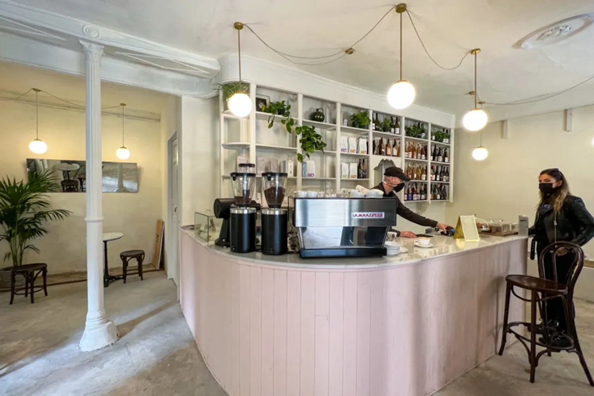 Bright, minimalist interior of Feliz Coffee Madrid with a curved pink service counter, professional espresso machine, and globe pendant lighting, providing a serene environment for productive study spots in Madrid.