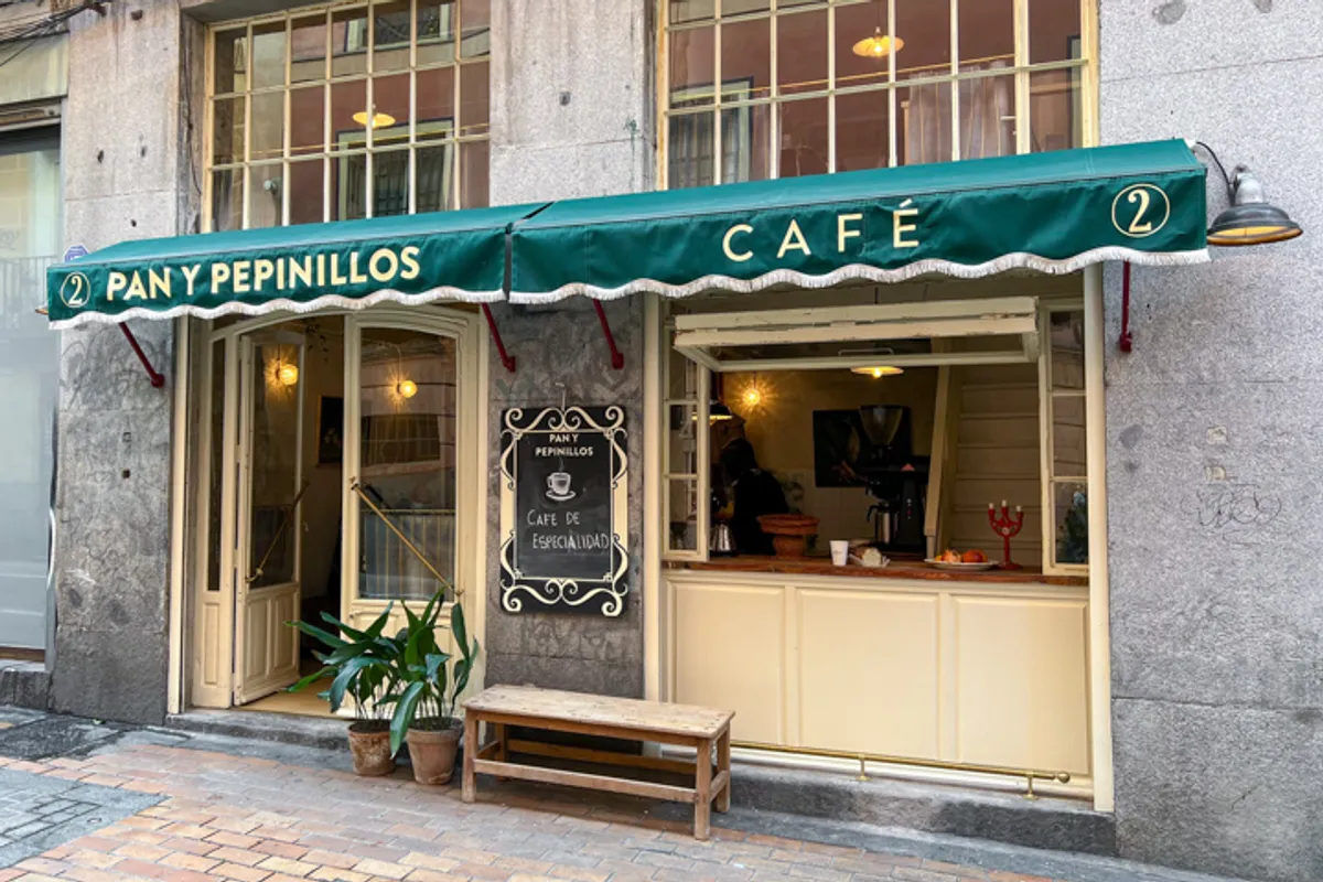 Charming exterior of Pan y Pepinillos, a specialty cafe in Madrid with a green awning and vintage wooden storefront, recognized as one of the best hidden study spots in Madrid.