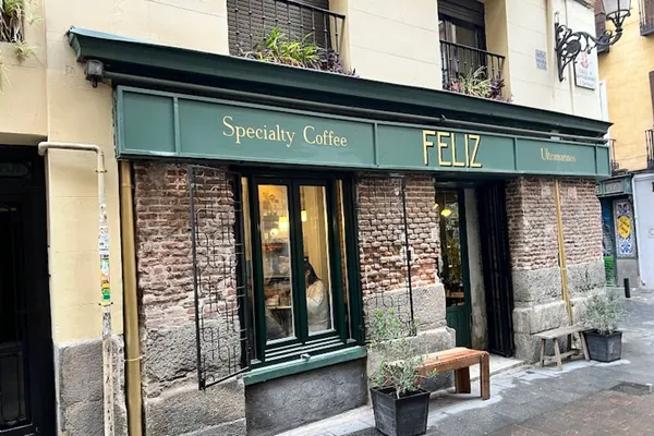 The rustic brick exterior of Feliz Coffee, a specialty cafe in Madrid located in the historic Barrio de las Letras, featuring a green vintage storefront and outdoor seating—ideal for those seeking quiet study spots in Madrid.
