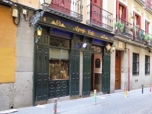 Exterior of Ajenjo Cafe, a vintage cafe in Madrid located on a narrow cobblestone street, known as one of the cozy study spots in Madrid with traditional green wooden shutters and warm lantern lighting.