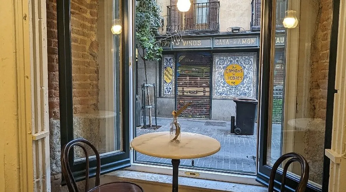 Bright, minimalist interior of Feliz Coffee Madrid with a curved pink service counter, professional espresso machine, and globe pendant lighting, providing a serene environment for productive study spots in Madrid.