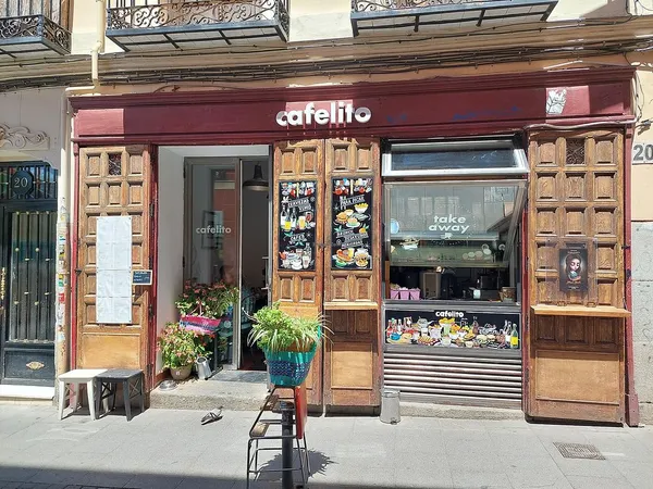 The rustic wooden storefront of Cafelito, a neighborhood cafe in Madrid with a "take away" window and eclectic menu boards, recognized as one of the authentic and quiet study spots in Madrid.