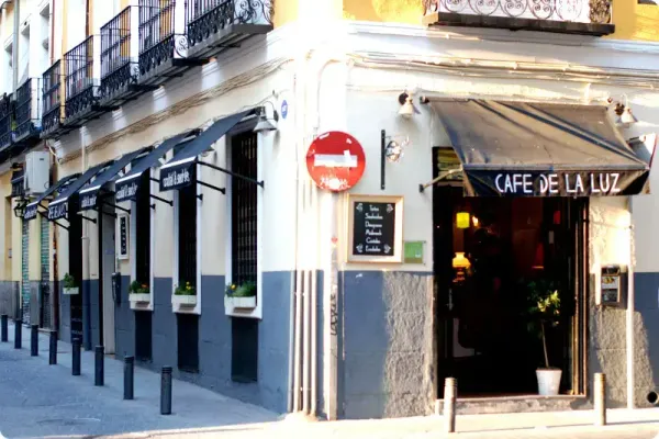 Corner view of Café de la Luz, a charming cafe in Madrid with black awnings and white flower boxes, situated on a pedestrian street and known as one of the most welcoming study spots in Madrid.
