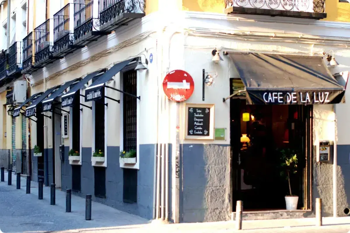 Corner view of Café de la Luz, a charming cafe in Madrid with black awnings and white flower boxes, situated on a pedestrian street and known as one of the most welcoming study spots in Madrid.