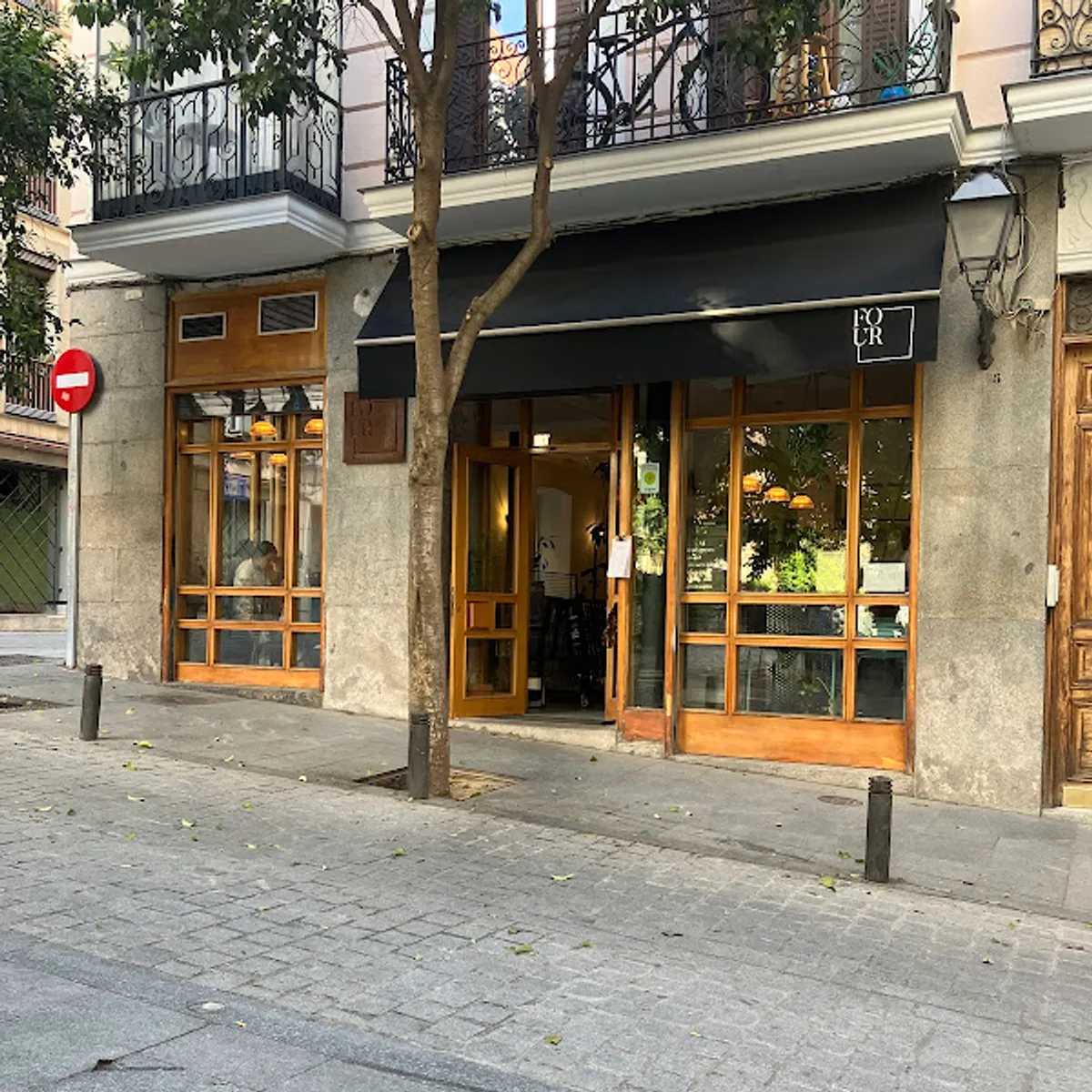 Exterior view of Four Specialty Coffee, a minimalist cafe in Madrid with a black awning and large wooden-framed windows, offering a quiet street-side atmosphere for those looking for local study spots in Madrid.