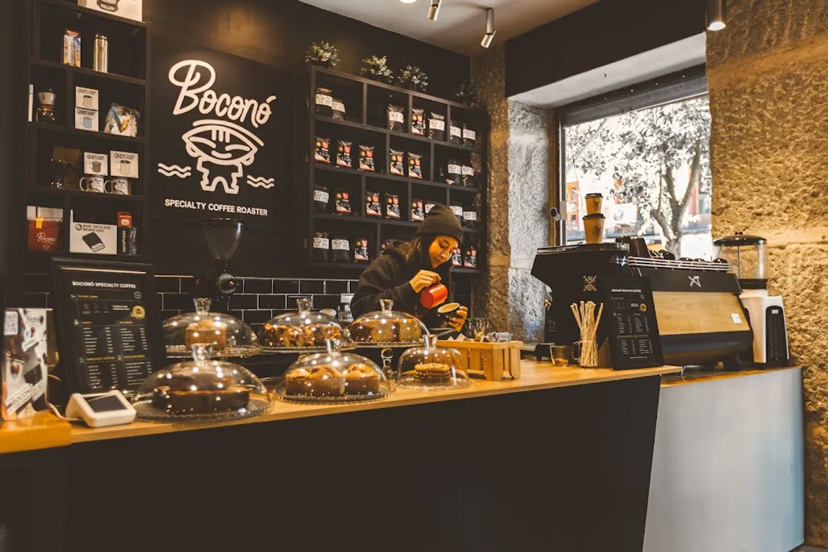Professional barista preparing latte art at Boconó Specialty Coffee Madrid, showing a sleek black service counter with fresh pastries and bagged coffee beans—a high-energy cafe in Madrid for specialty coffee lovers.
