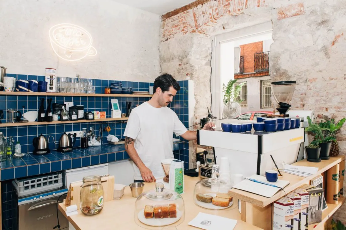A barista preparing specialty coffee at Hola Coffee, a minimalist cafe in Madrid with blue tiled walls and an industrial-chic aesthetic—a top-rated choice for those seeking quiet study spots in Madrid.