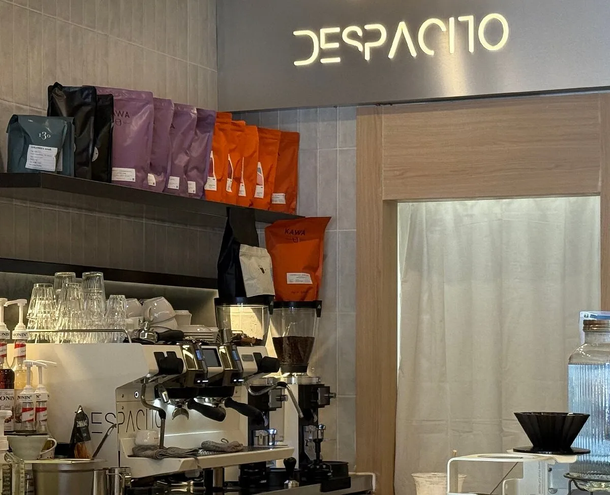 Modern service station at Despacito Coffee Madrid, showcasing a high-end espresso machine, colorful bags of specialty coffee beans, and bright neon signage in a contemporary cafe in Madrid.