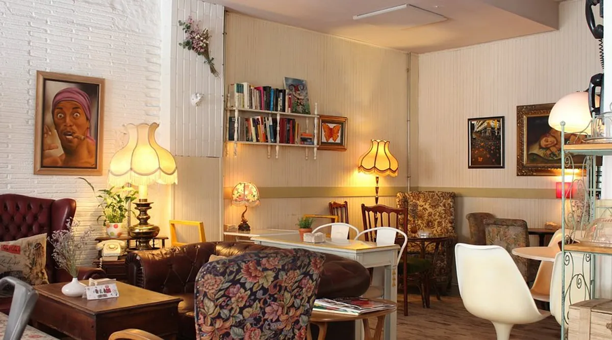 The cozy, living-room style interior of Café de la Luz Madrid, featuring vintage leather sofas, floral armchairs, and warm lamp lighting, perfect for those seeking comfortable study spots in Madrid.