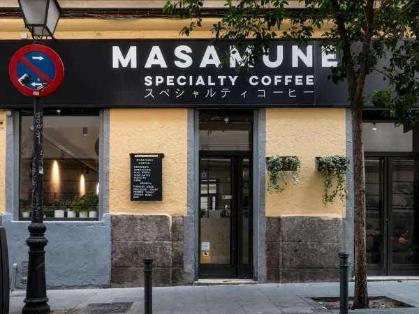 Modern storefront of Masamune Specialty Coffee in Madrid featuring a bright yellow facade, Japanese-inspired minimalist branding, and a window menu—a top-rated choice for those seeking specialty cafe Madrid experiences in Malasaña.