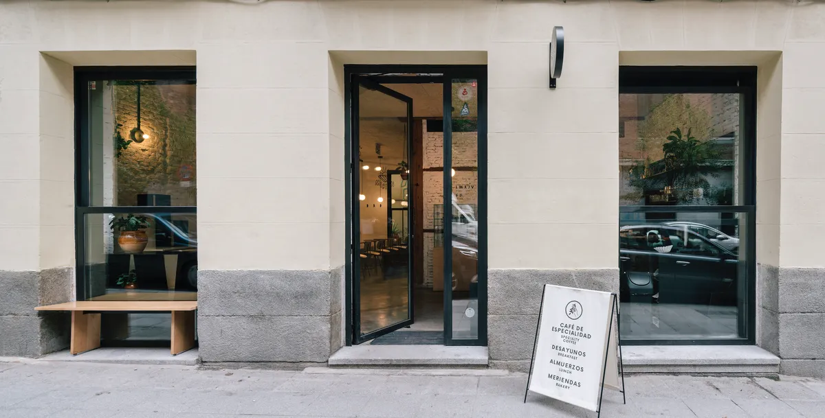 Minimalist white storefront of Misión Café, a premier specialty cafe in Madrid with large glass windows and an outdoor menu board—a popular choice for high-quality coffee and quiet study spots in Madrid.