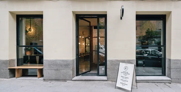 Minimalist white storefront of Misión Café, a premier specialty cafe in Madrid with large glass windows and an outdoor menu board—a popular choice for high-quality coffee and quiet study spots in Madrid.